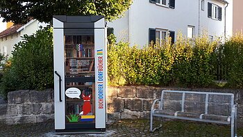 Öffentlicher Bücherschrank in der Hauptstraße in Buchdorf Blick auf den öffentlich zugänglichen Bücherschrank in der Hauptstraße in Buchdorf mit rechts daneben stehender Sitzgelegenheit.