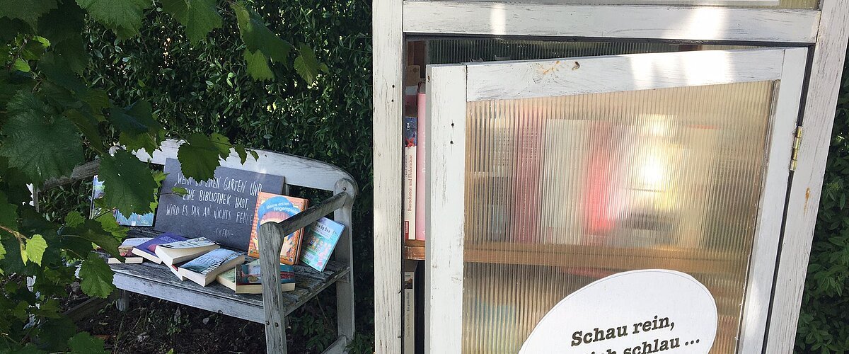 Blick auf den öffentlich zugänglichen Bücherschrank in der Bürgermeister-Rößner-Straße 1 in Buchdorf mit daneben stehender Sitzgelegenheit.