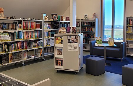 Blick auf gut befüllte Bücherregale in der Bücherei in Buchdorf. Rechts im Bild sieht man eine Sitzgruppe.