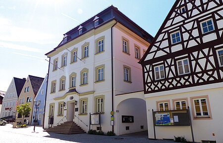 Straßenansicht der Monheimer Innenstadt: Im Vordergrund das Rathaus der Stadt Monheim, mit weiteren mehreren Gebäuden, darunter ein Fachwerkhaus, das man Schindlerhaus nennt.