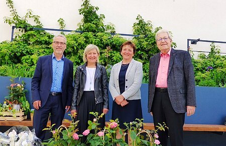 Verabschiedungsfeier der Verwaltungsgemeinschaft Monheim Vier Personen stehen vor einer bepflanzten Mauer mit Rosen und anderen Blumen im Vordergrund.