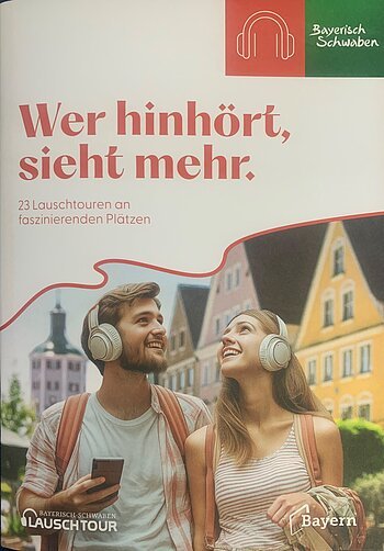 Titelblatt der Broschüre "Wer hinhört, sieht mehr" zu Lauschtouren vom Tourismusverband Allgäu/Bayerisch-Schwaben e.V.. Auf dem Foto zwei junge Personen mit hellen Kopfhörern und Rucksäcken vor bunten Häusern in einer Stadt in Bayern. Auf dem Foto der Text "23 Lauschtouren an faszinierenden Plätzen".