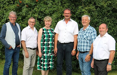 Verabschiedung Gerhard Leinfelder Sechs Personen stehen nebeneinander vor grünen Bäumen, alle blicken in die Kamera und lächeln.