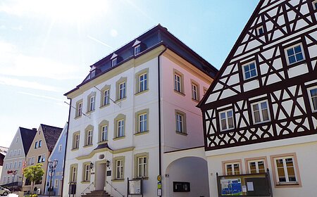 Straßenansicht der Monheimer Innenstadt: Im Vordergrund das Rathaus der Stadt Monheim, mit weiteren mehreren Gebäuden, darunter ein Fachwerkhaus, das man Schindlerhaus nennt.