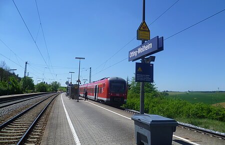 Bahnhof Otting-Weilheim Der Bahnhof Otting-Weilheim mit rotem Zug auf dem Gleis, blauer Himmel, grüne Landschaft im Hintergrund.